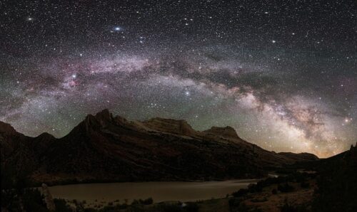 A photograph of the milky way with mountains as the horizon to emphasise how immense the galaxy is