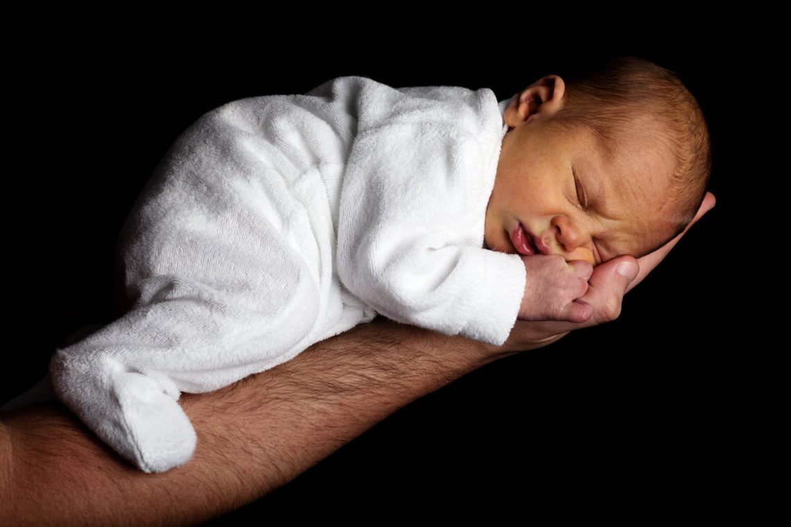 A photo of a newborn baby just a few days old lying asleep on his father's arm