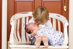 A photograph of a newborn being held and cuddled by an older sibling