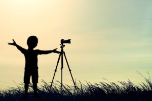 Silhouette of a young photographer with camera mounted on tripod
